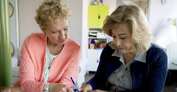 Zittend aan tafel helpt een medewerkster een vrouw bij het indienen van een aanvraag.